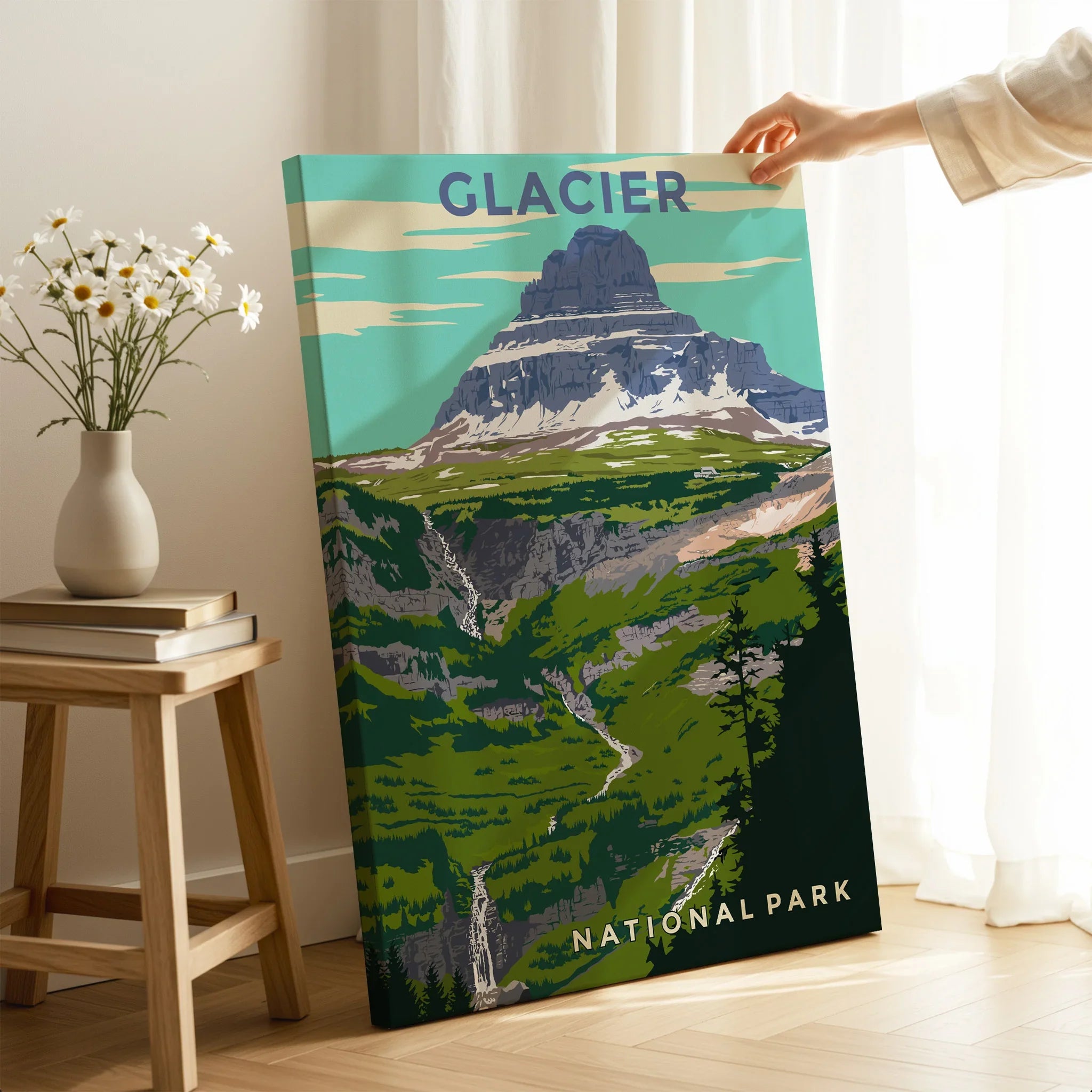 Hand holding Glacier National Park canvas art in bright modern room with wildflower vase