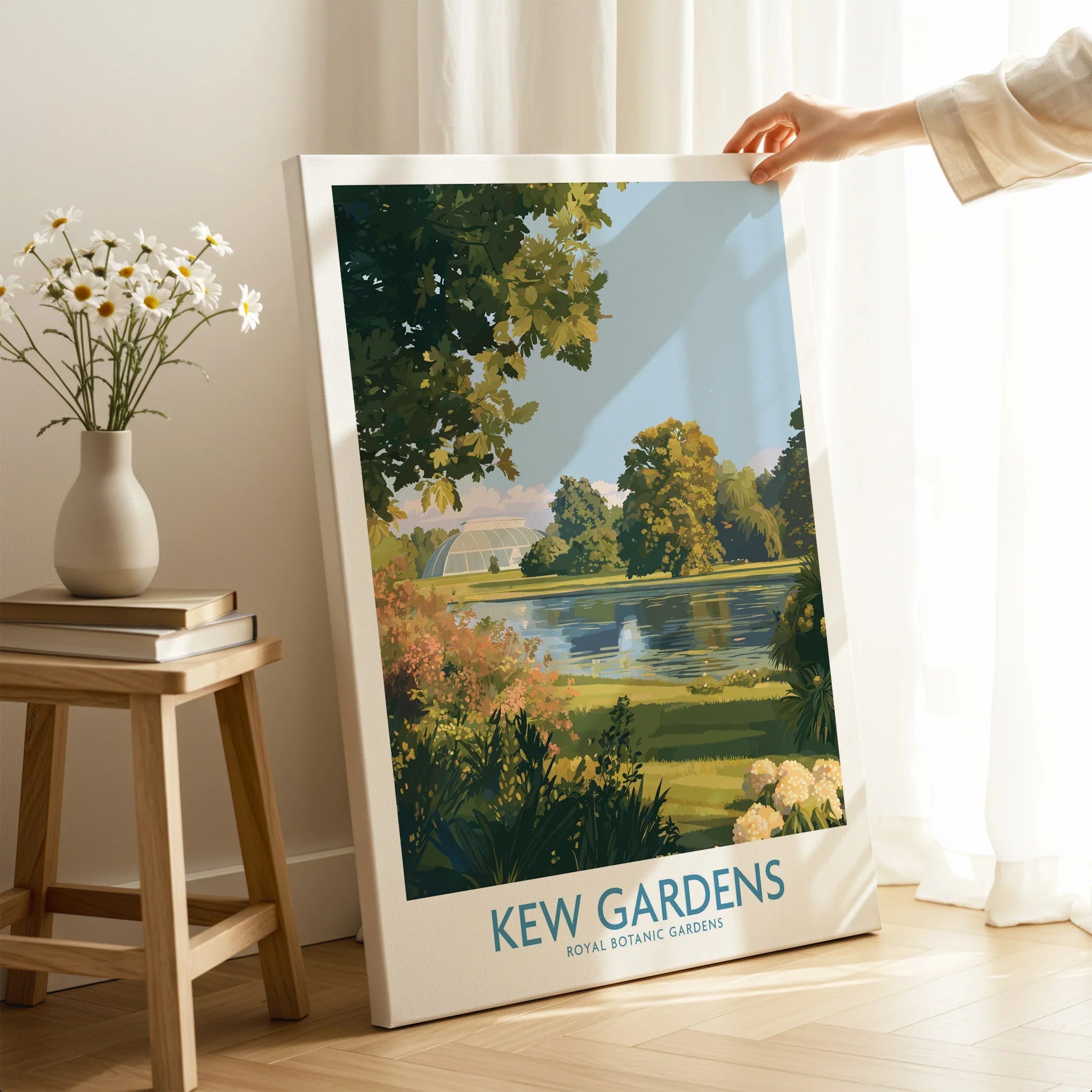 Hand holding Kew Gardens travel poster canvas print in bright, modern room with vase and books.