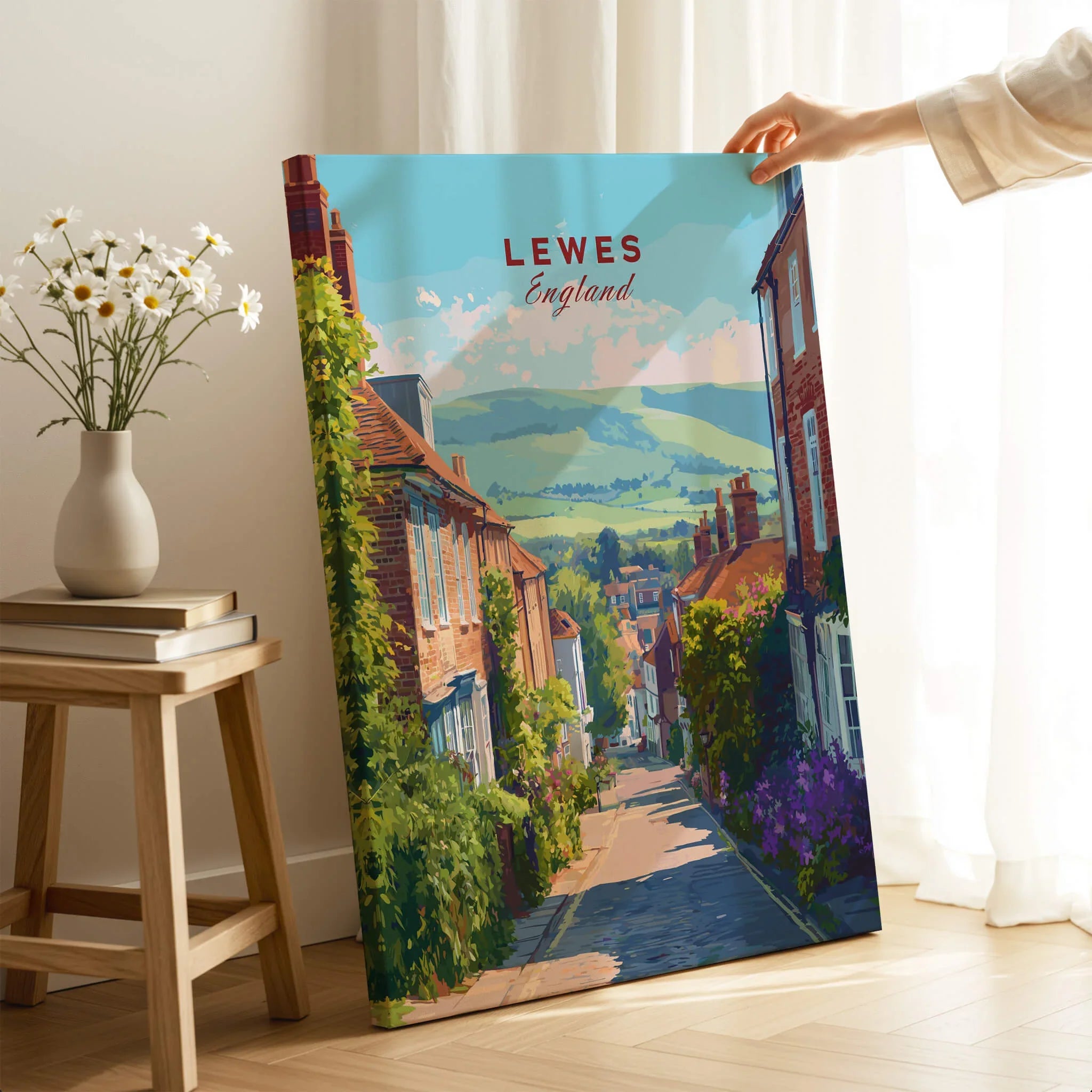 Hand holding Lewes England travel poster canvas print in bright room with flowers and books