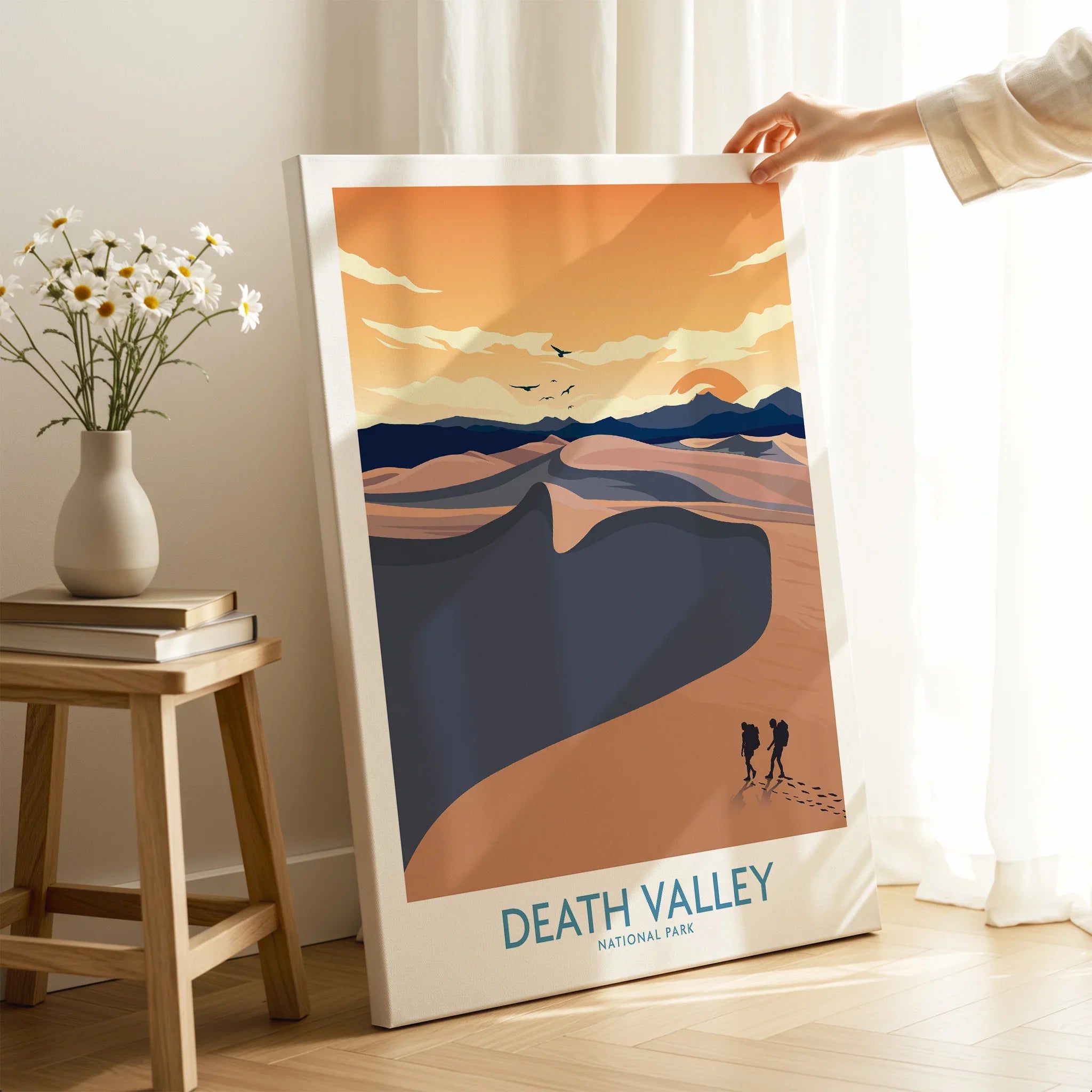Hand holding Death Valley National Park canvas print in modern room with flowers and books
