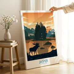 Hand holding Jasper National Park canvas print with moose and mountain lake artwork in cozy room.