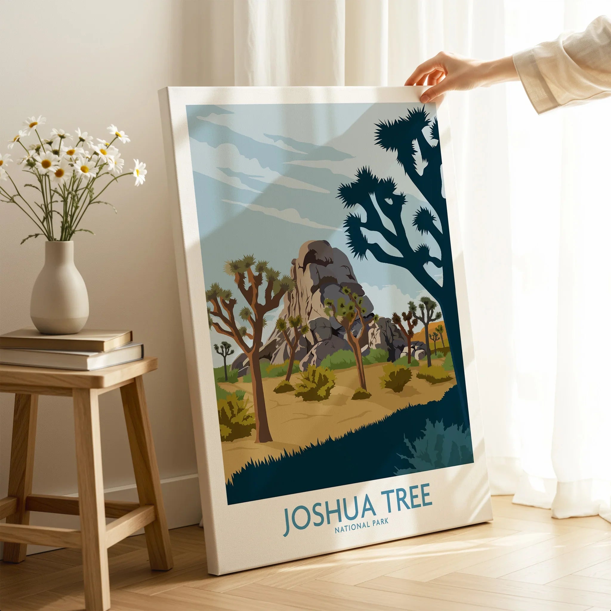 Hand holding Joshua Tree National Park canvas wall art in a bright room with vase and books