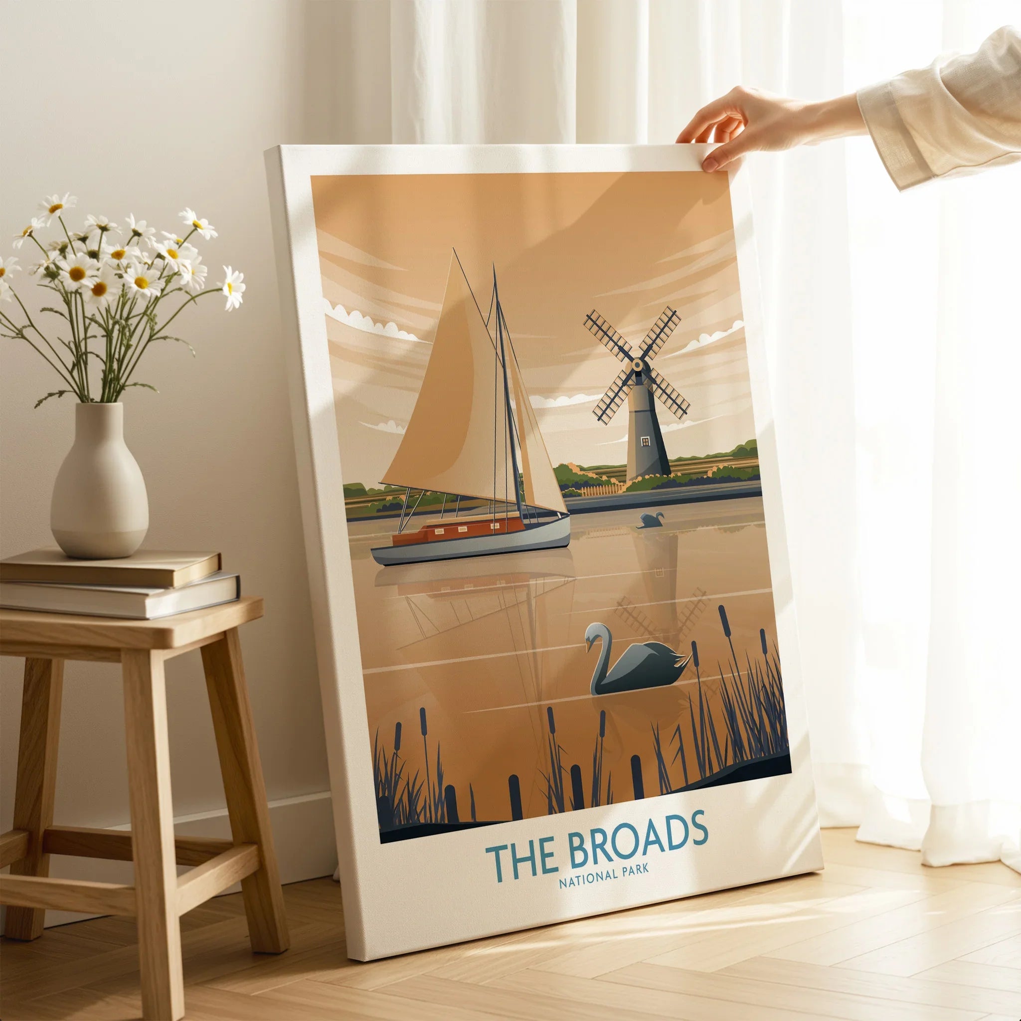 Hand holding canvas print of The Broads National Park travel poster with sailboat, swan, windmill.