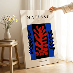 Matisse Art Prints -  Red Coral Black Leaves Blue Frame Poster displayed on wall next to a vase of flowers.