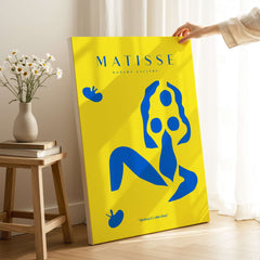 Matisse Art Prints - Blue Nude Abstract Figure Yellow Poster displayed in a bright interior with flowers and a wooden table.