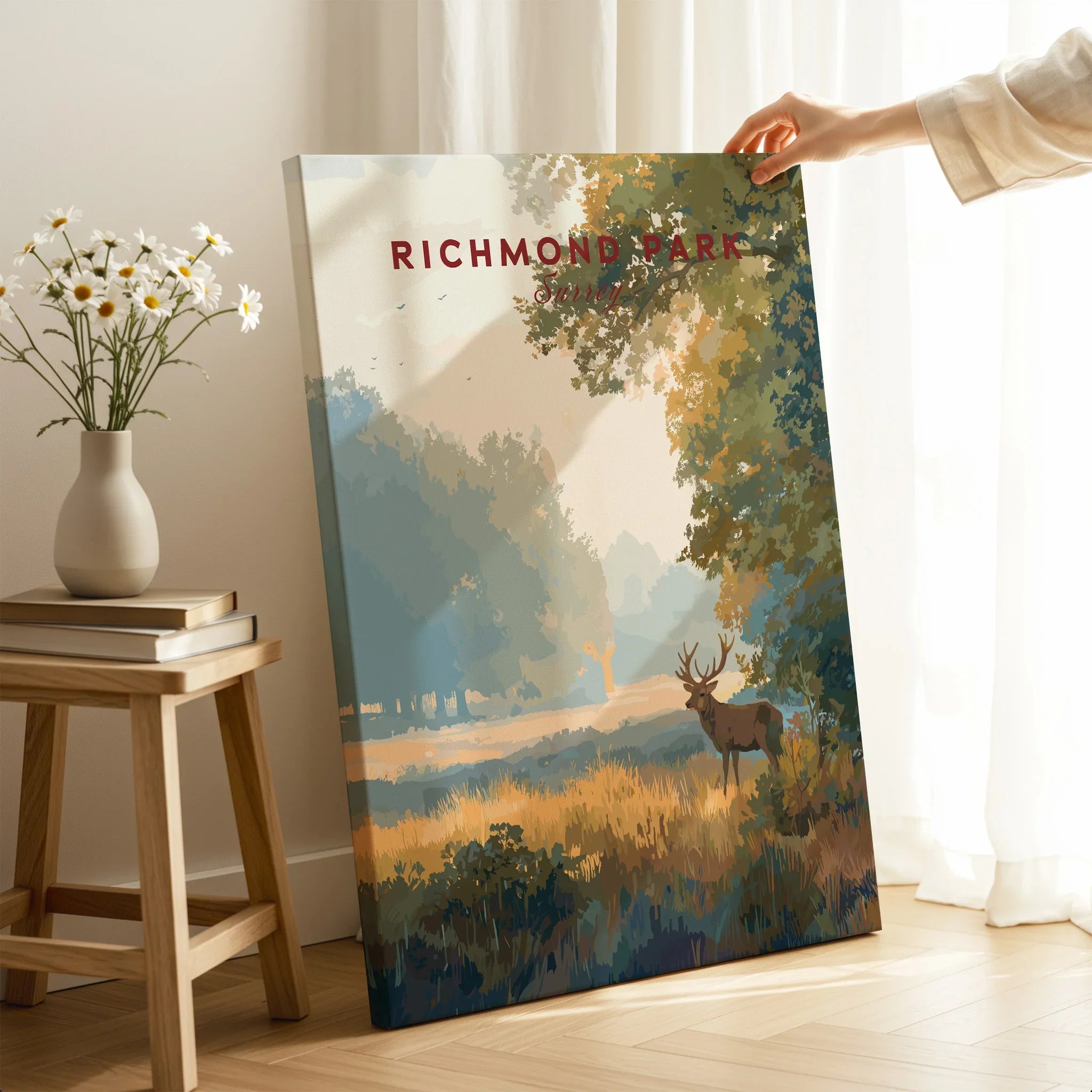 Hand holding a Richmond Park travel poster canvas print with deer and trees in a modern room