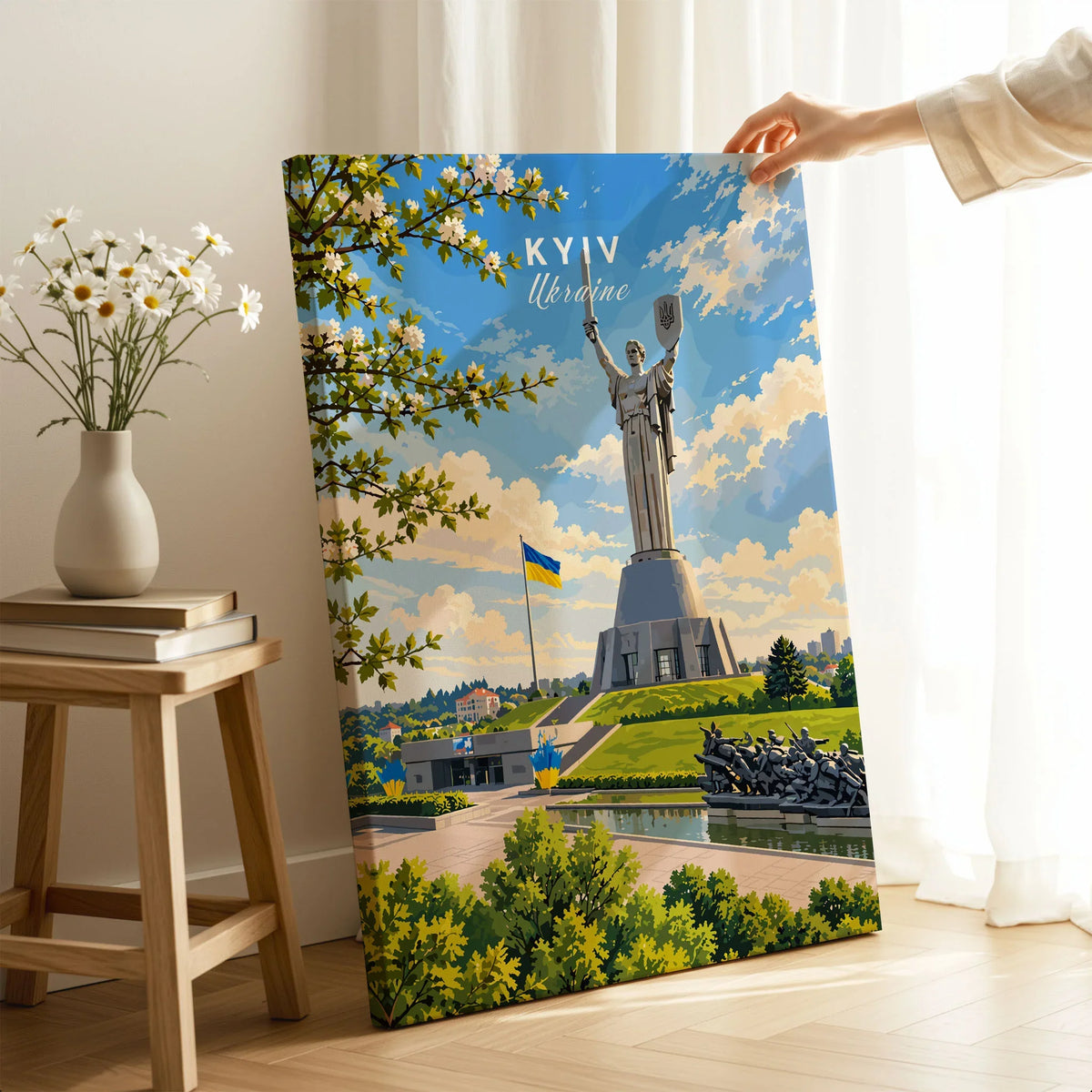 Kyiv Ukraine Motherland Monument Travel Poster — the Motherland Monument under spring blossom with the Ukrainian flag flying, shown as canvas print mirror edge hand holding room setting