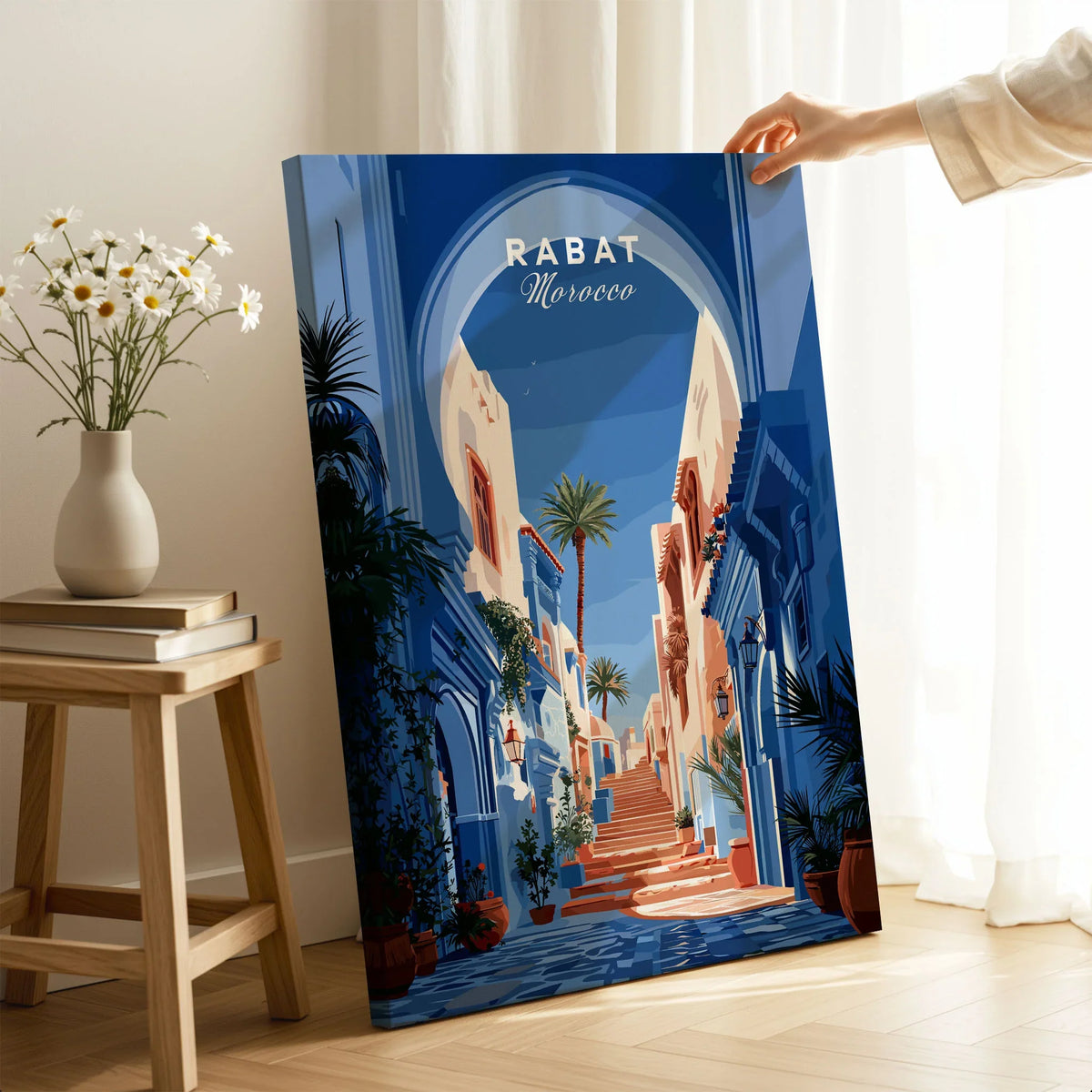 Rabat Morocco Blue Medina Travel Poster — a blue-washed medina lane and stone steps seen through a horseshoe arch, shown as canvas print mirror edge hand holding room setting