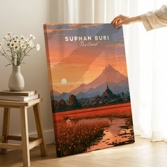 Suphan Buri Thailand Lotus Lake Travel Poster — a lotus-covered lake and temple spire at sunset beneath a mountain peak, shown as canvas print mirror edge hand holding room setting