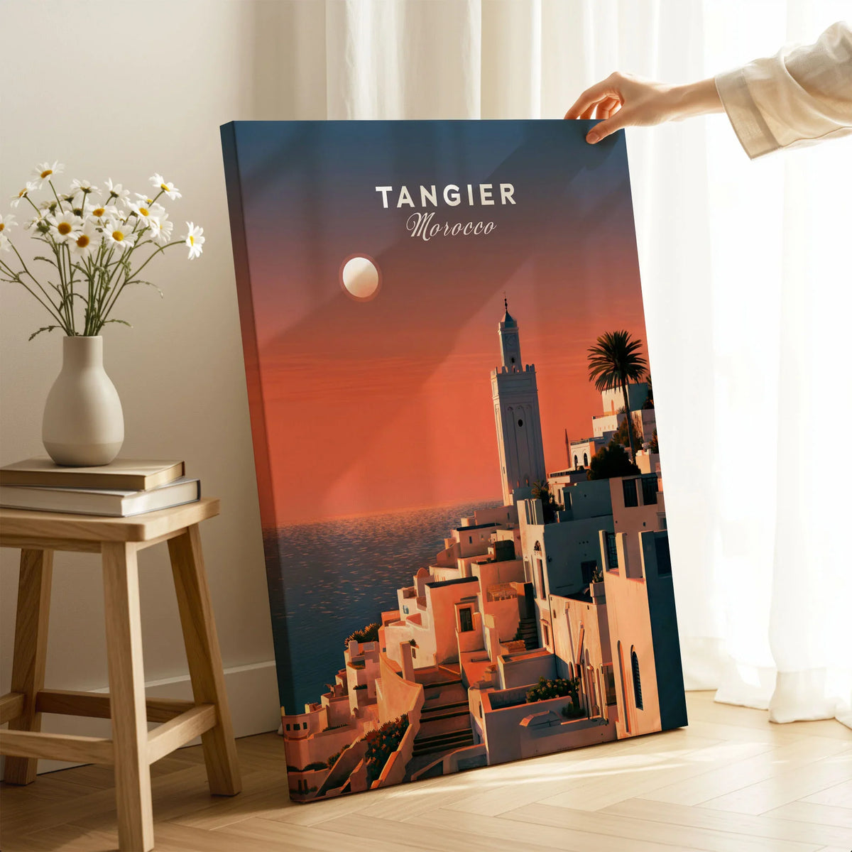 Tangier Morocco Golden Hour Travel Poster — a whitewashed hillside town and minaret glowing above the sea at sunset, shown as canvas print mirror edge hand holding room setting