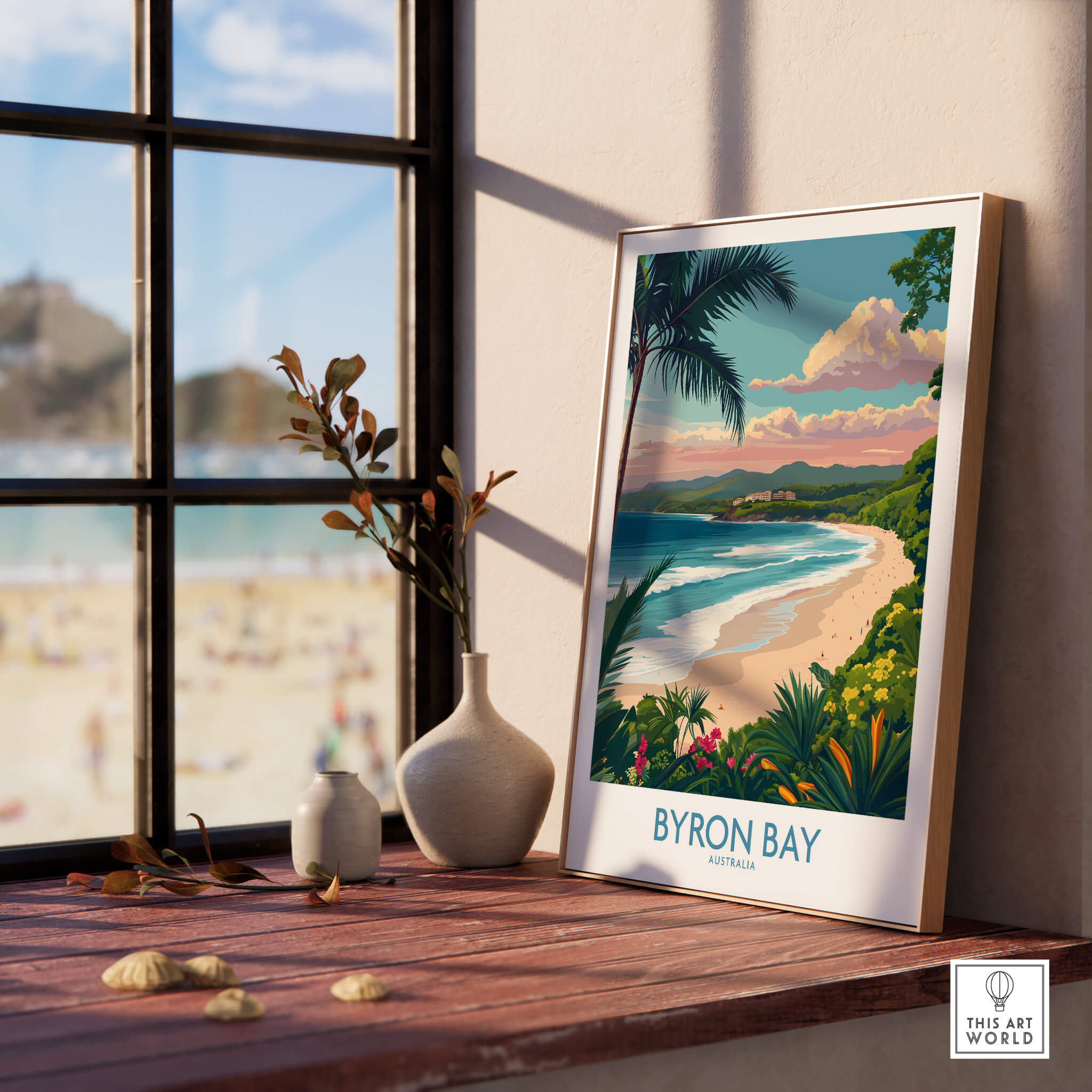 Byron Bay Poster - Australia Wall Art displayed on a wooden table beside a window showcasing the coastal landscape.