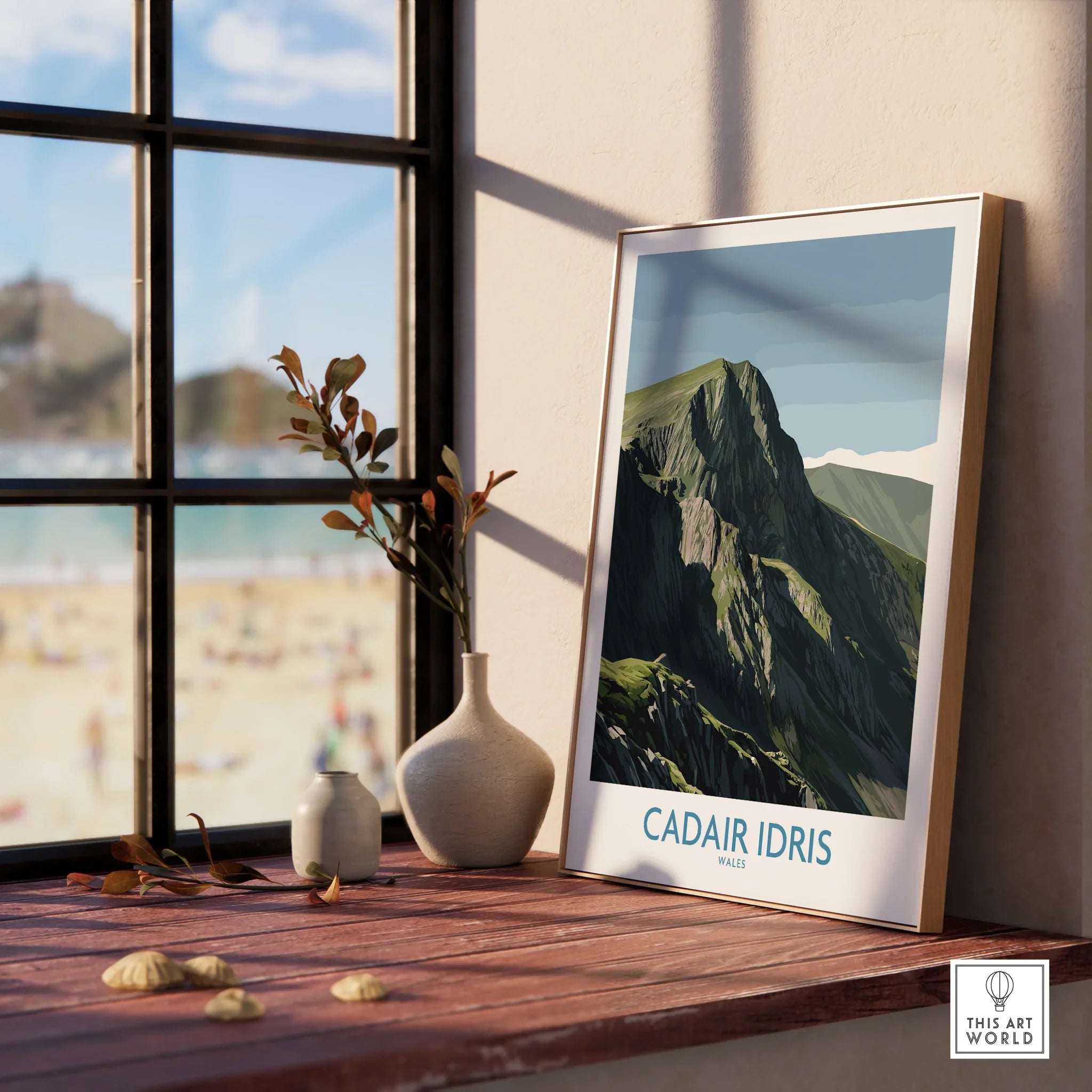 Framed Cadair Idris mountain travel poster on windowsill with vases, beach view outside