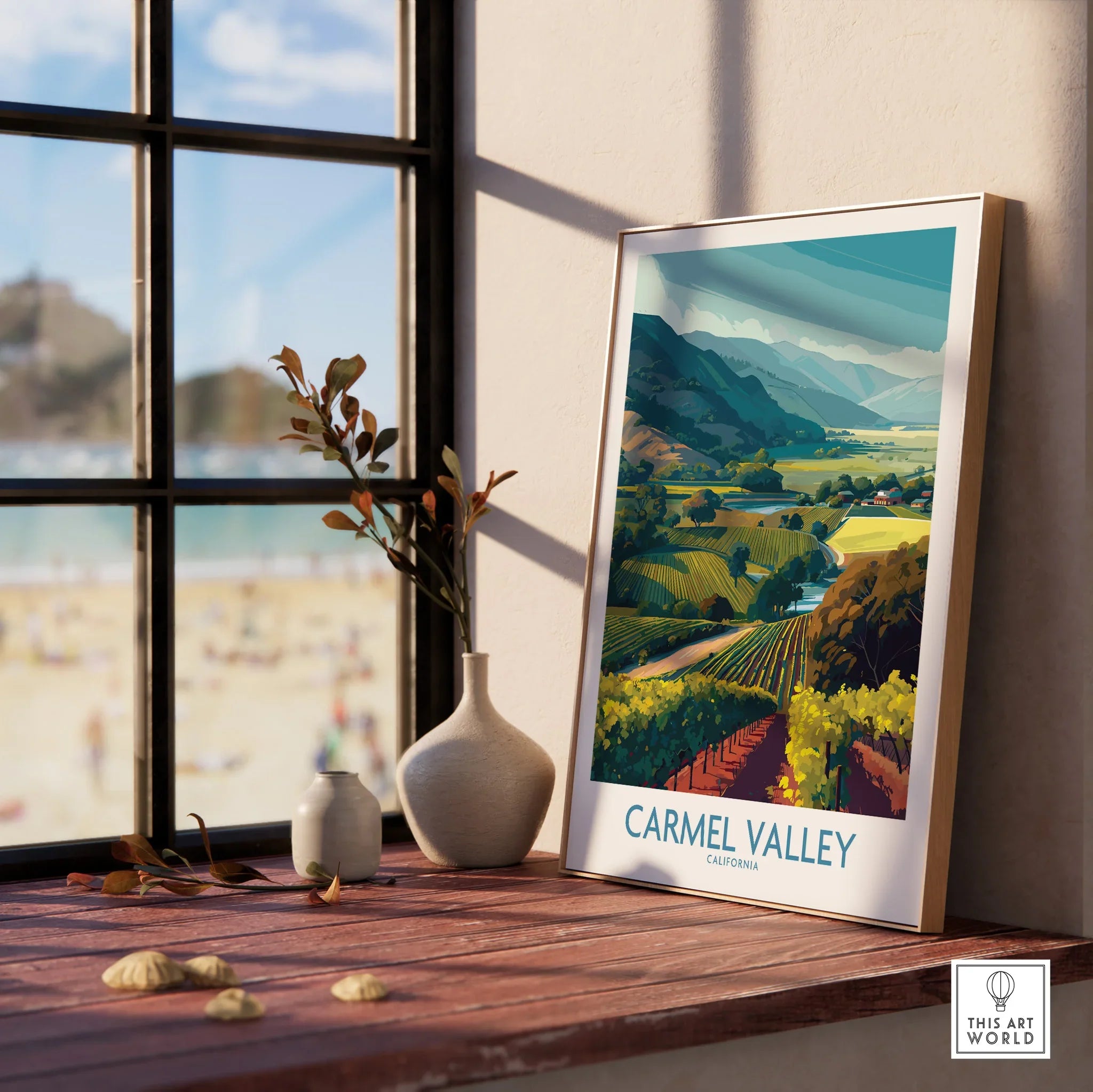 Framed Carmel Valley travel poster with vineyard art on a window sill, coastal view outside.