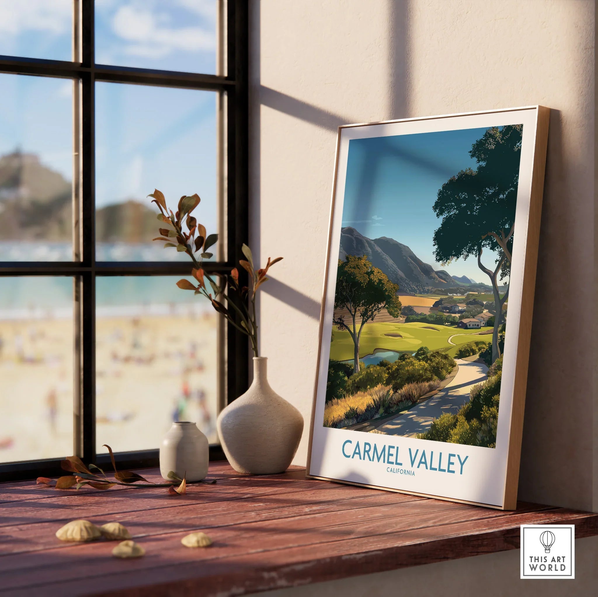 Framed Carmel Valley travel poster on a sunlit windowsill with beach view and ceramic vases.