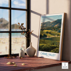 Framed Carmel Valley travel poster with vineyard landscape on a sunny windowsill, next to vases.