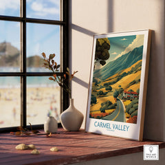Framed Carmel Valley travel poster on windowsill with beach view and decorative vases.