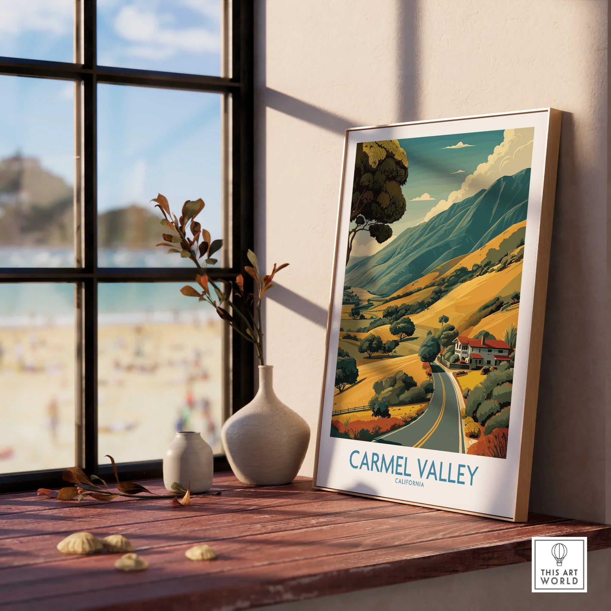 Framed Carmel Valley travel poster on windowsill with beach view and decorative vases.