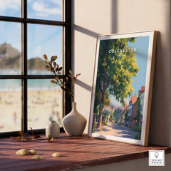 Colchester England travel poster in natural wood frame on windowsill with vases and beach view