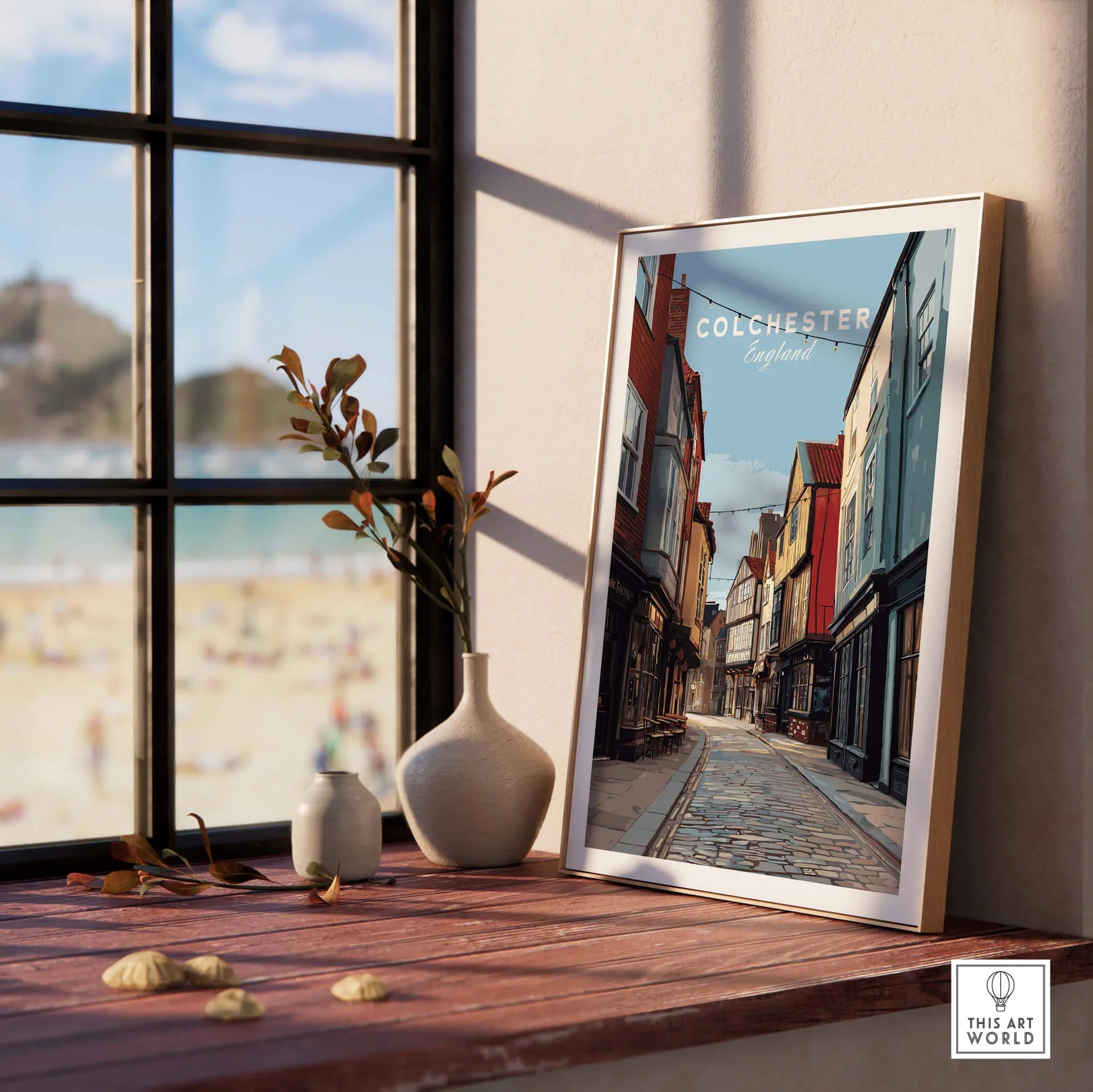 Colchester England travel print in natural wood frame on windowsill with vases, beach view outside