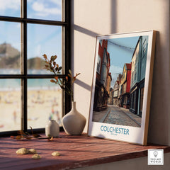 Framed Colchester travel poster on windowsill with coastal view and decorative vases