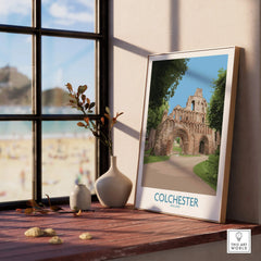 Framed Colchester travel poster on window sill with vases and beach view in background
