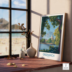Framed Greenwich London travel poster with natural wood frame on a windowsill, beach view outside