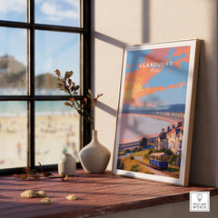 Framed Llandudno Wales travel poster on windowsill with vases, beach view outside