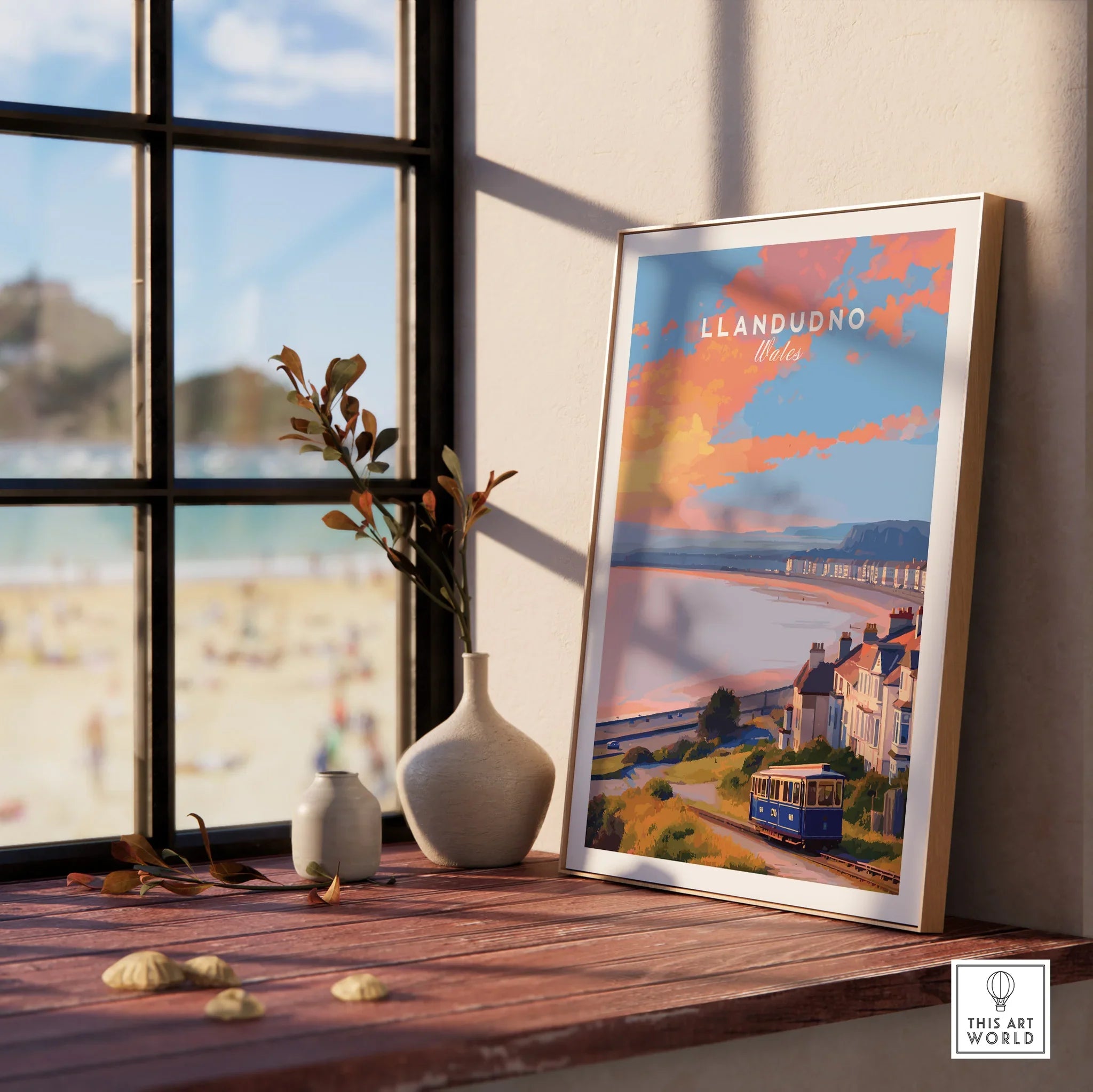 Framed Llandudno Wales travel poster on windowsill with vases, beach view outside