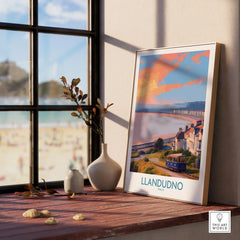Framed Llandudno travel poster on a window sill with beach view and natural wood frame