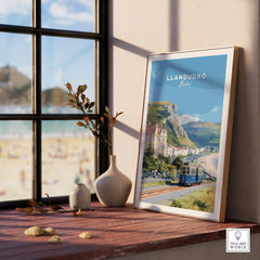 Framed Llandudno Wales travel poster with tram, beach and coastal view on window sill.