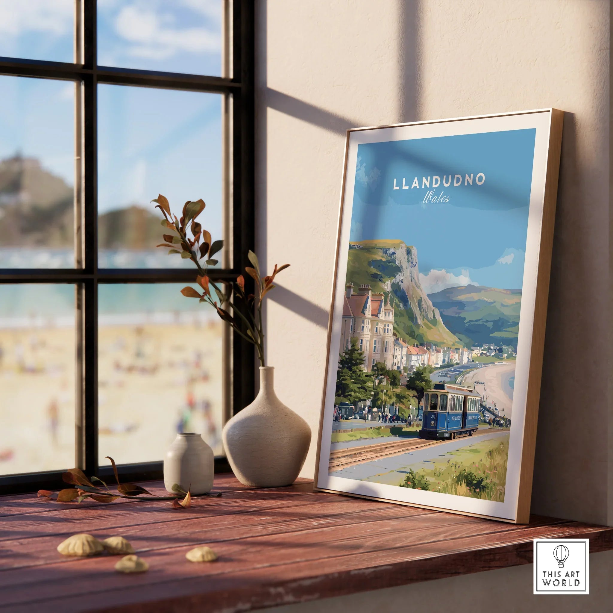 Framed Llandudno Wales travel poster with tram, beach and coastal view on window sill.