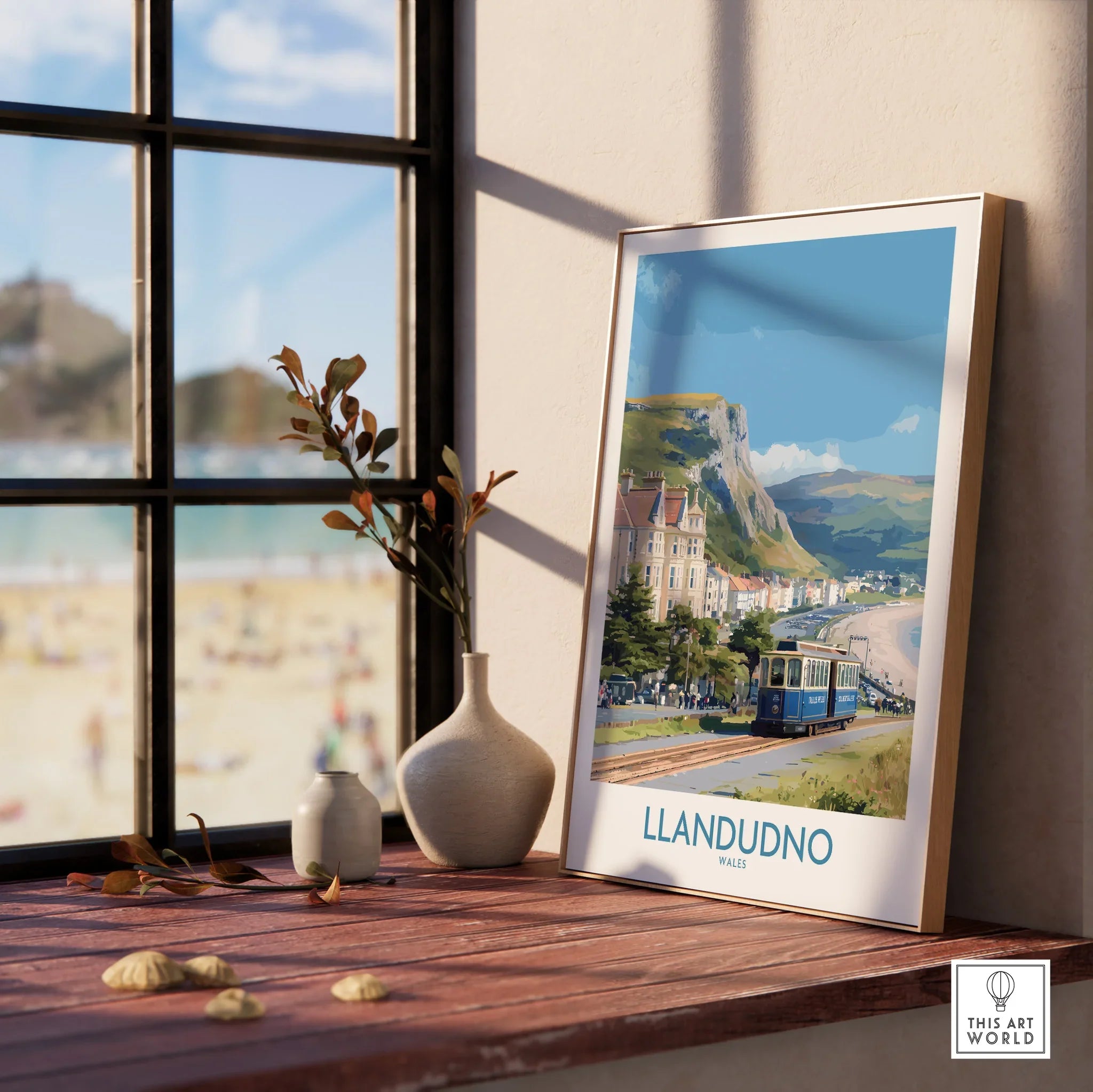Llandudno travel poster framed in natural wood, on a windowsill with beach view and vases.