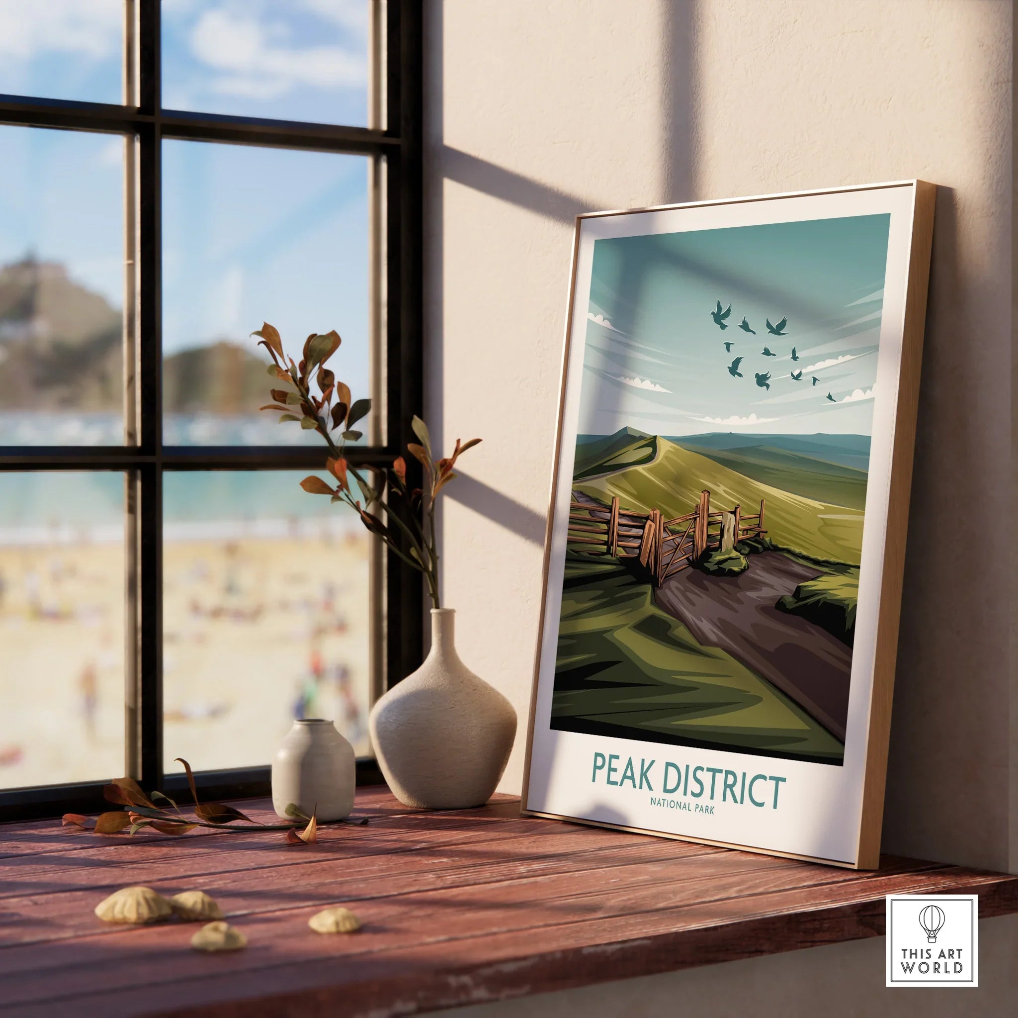 Framed Peak District National Park print on a wooden windowsill with vases and beach view