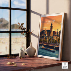 Framed Nijmegen city travel poster on windowsill with natural wood frame, beach view outside