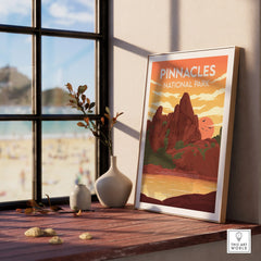 Framed Pinnacles National Park poster on windowsill with vases and beach view outside window.