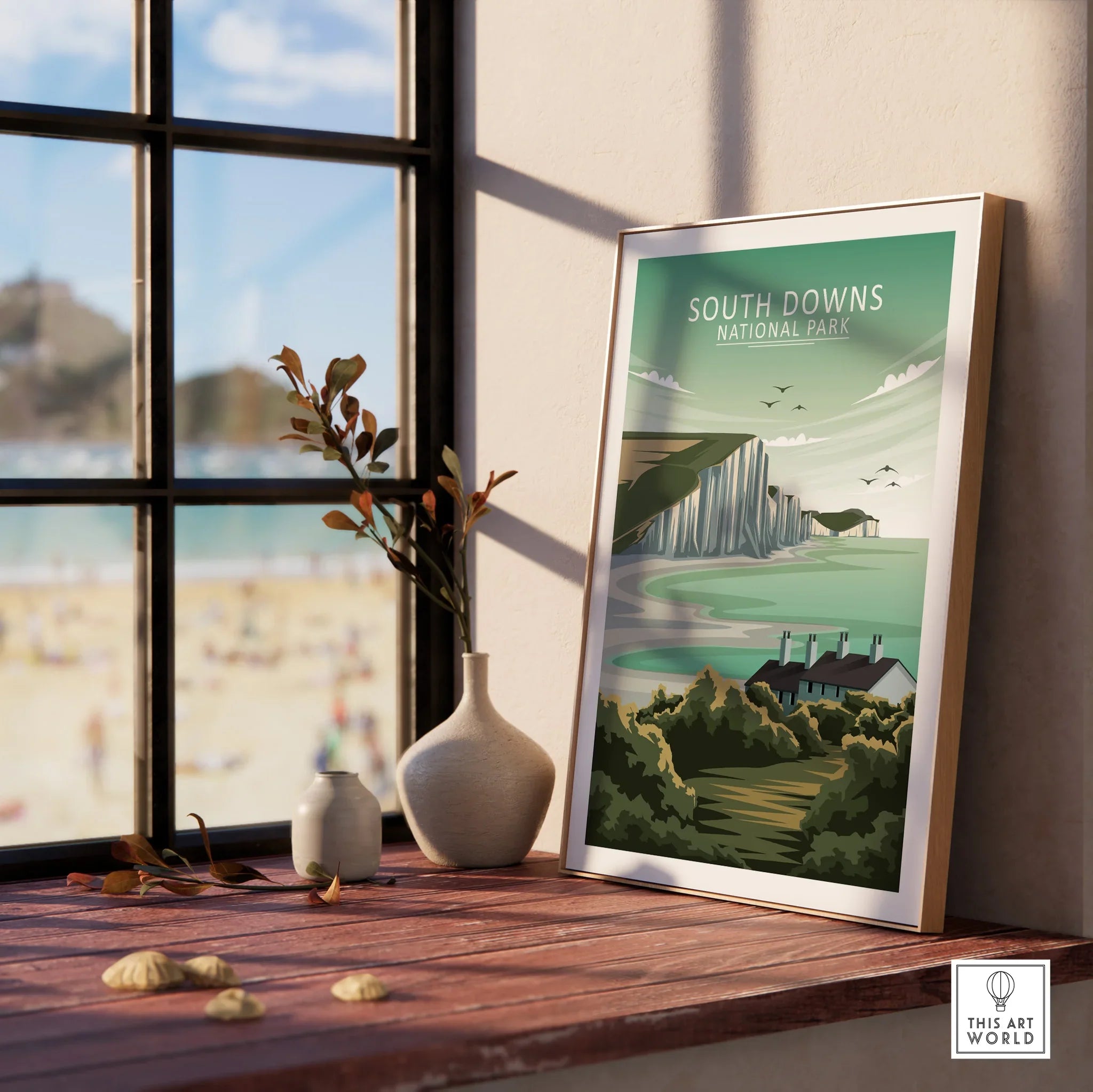 Framed South Downs National Park travel poster on windowsill with vases and beach view
