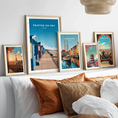 Frinton-on-Sea Travel Poster – Essex Coastline Beach Huts & Prom Art in a gallery wall set of five framed travel prints in natural wood frames above a bed