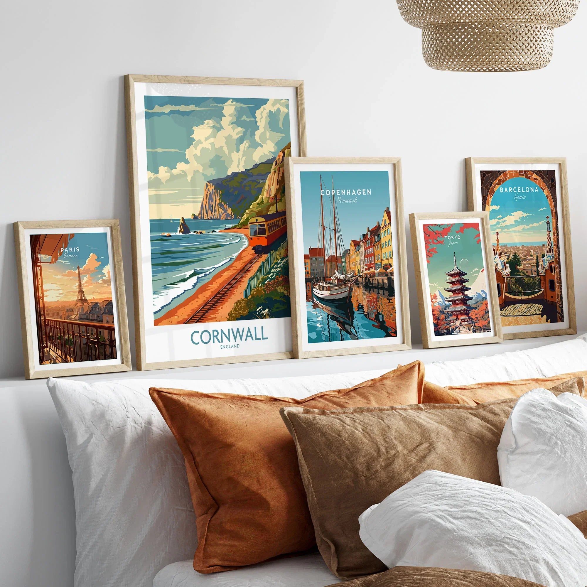 Cornwall Coast Wall Art Print in a gallery wall set of five framed travel prints in natural wood frames above a bed