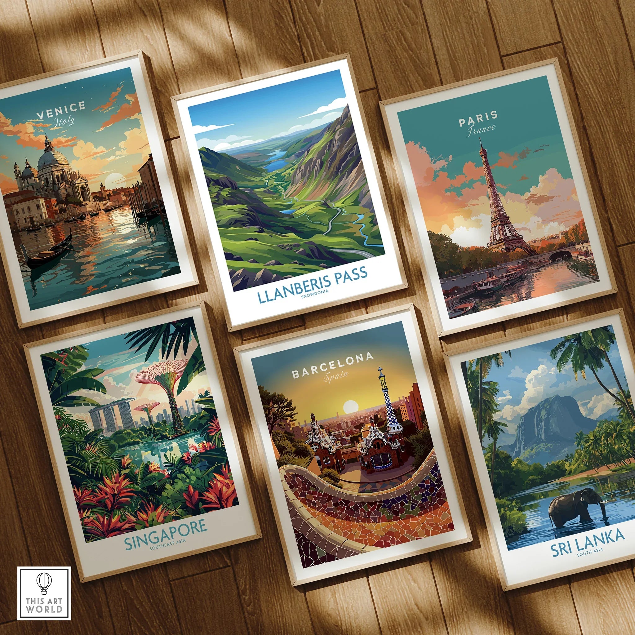 Set of six travel posters in wooden frames featuring Venice, Paris, Singapore, Barcelona, Sri Lanka, and Llanberis Pass, displayed on a wooden floor.