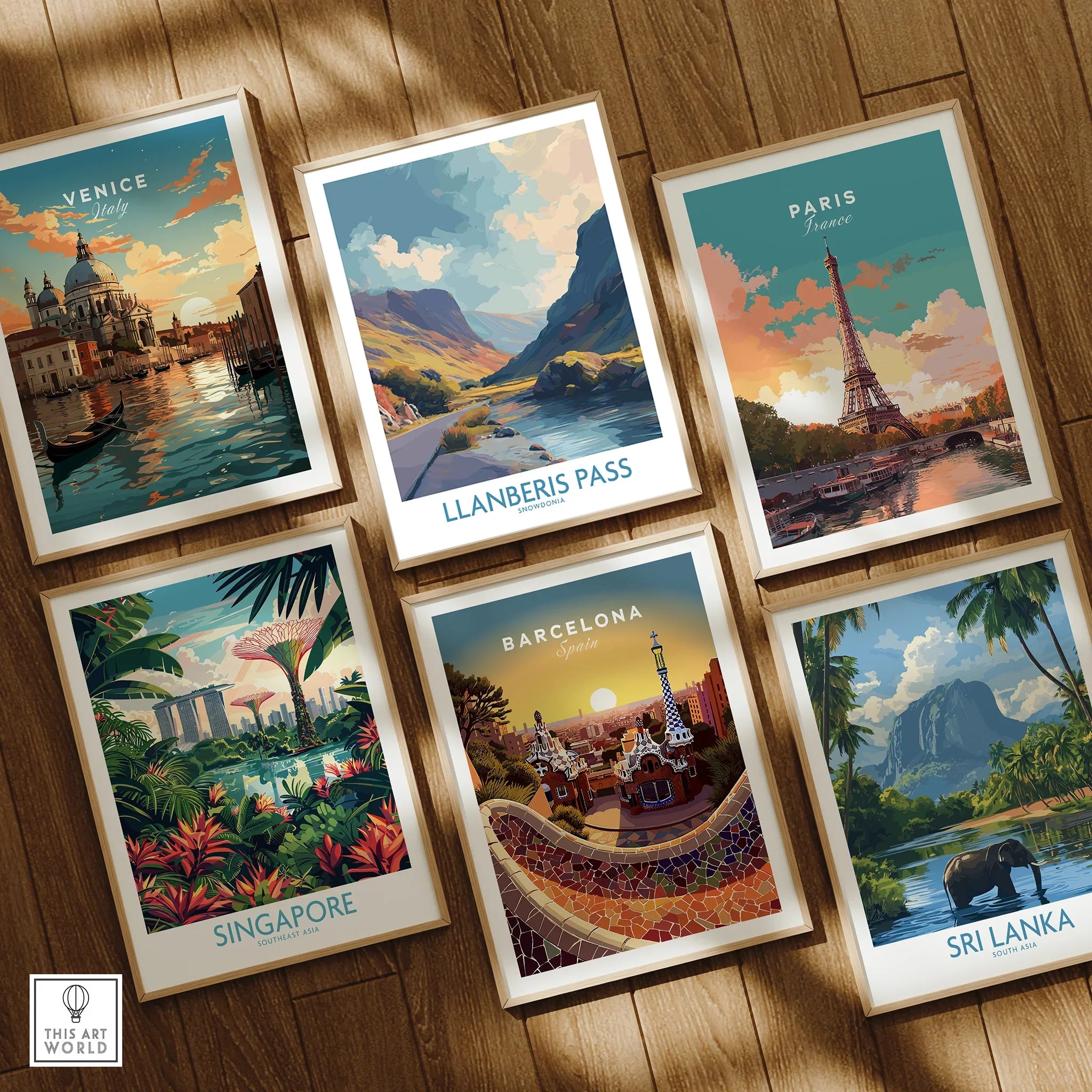 Set of six framed travel posters featuring Venice, Paris, Singapore, Barcelona, Sri Lanka, and Llanberis Pass, arranged on a wooden floor.