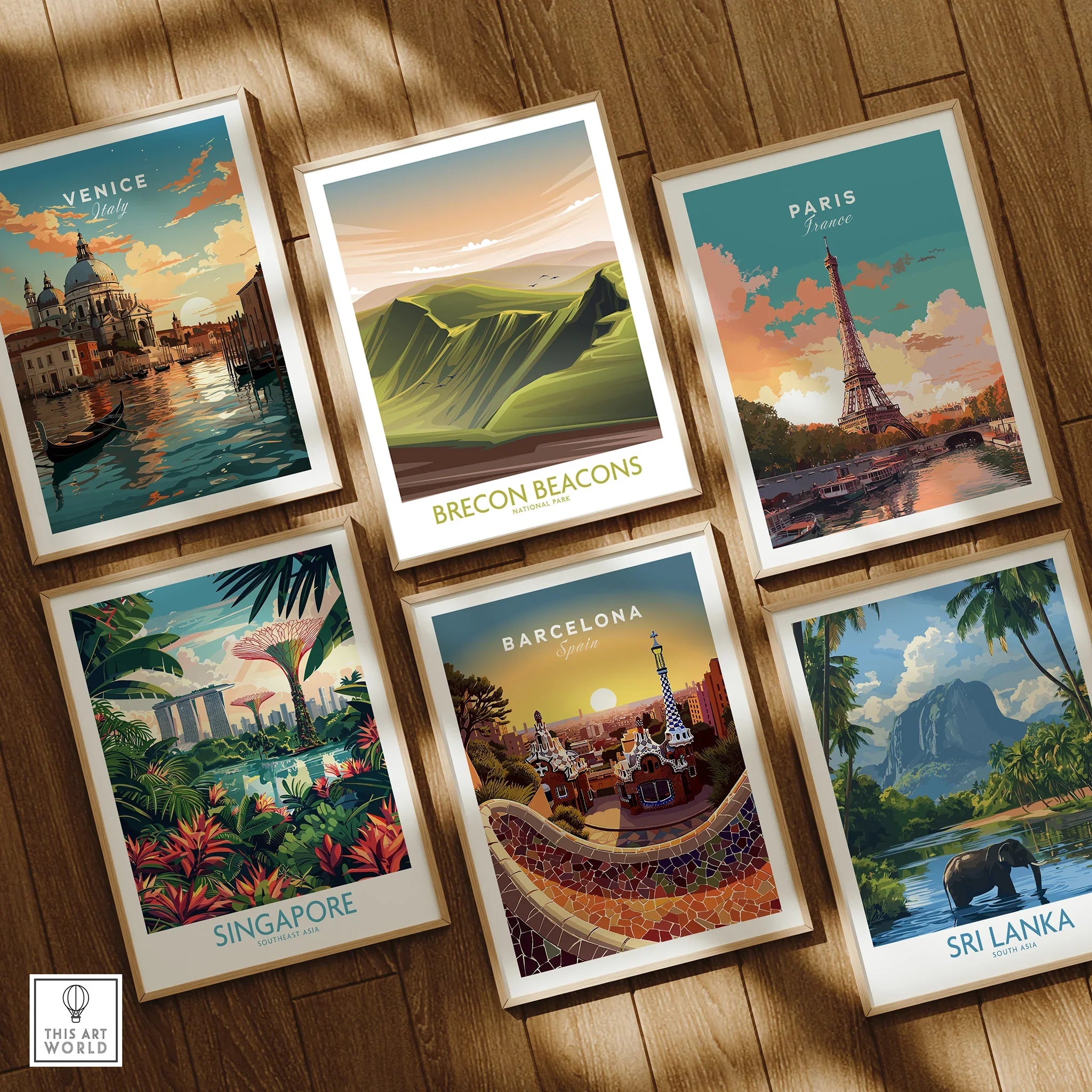 Set of six framed travel art prints on wooden floor featuring Venice, Paris, Singapore, Barcelona, Brecon Beacons, and Sri Lanka illustrations.