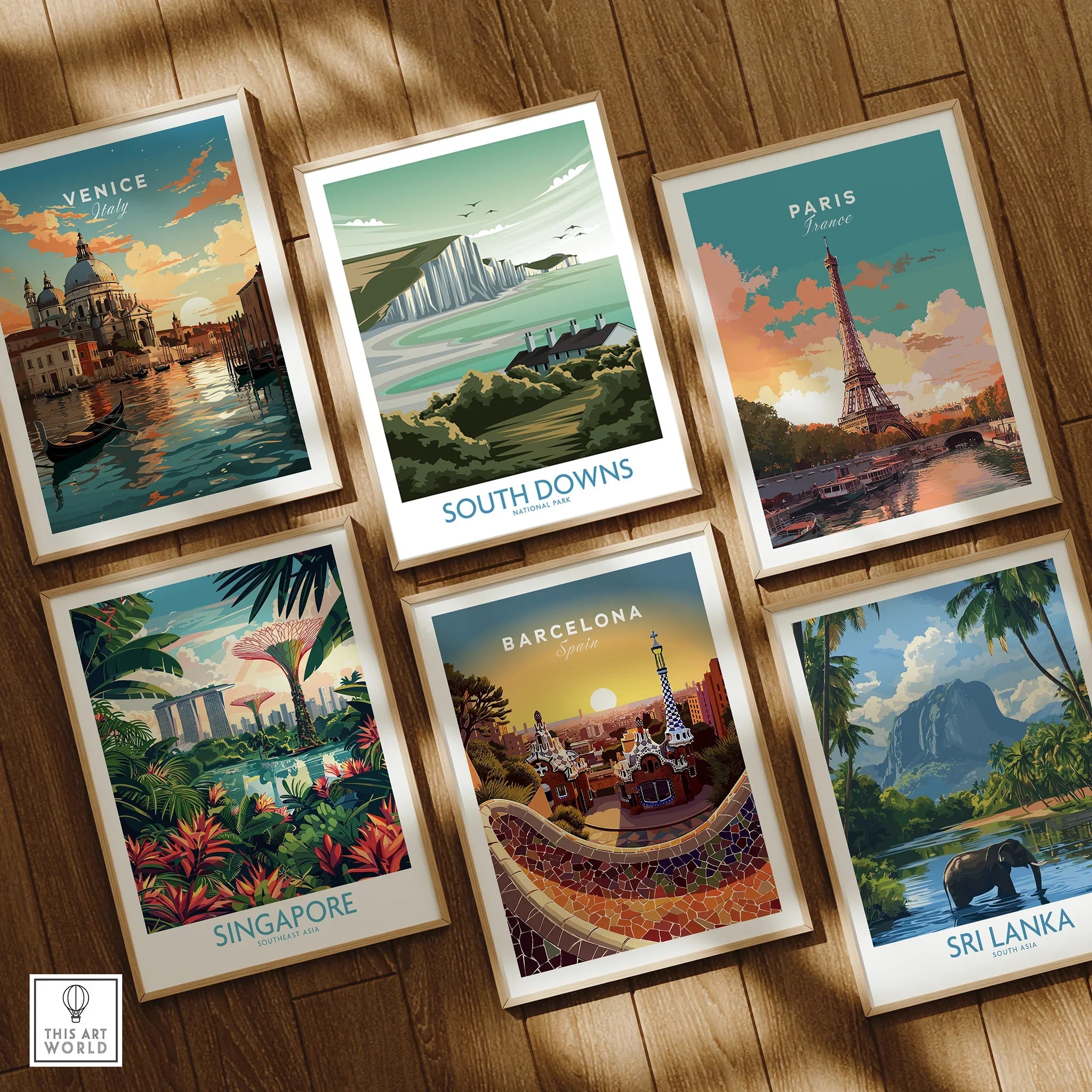 Set of six framed travel poster prints on wooden floor, featuring Venice, Paris, Barcelona, Singapore, Sri Lanka, and South Downs National Park.