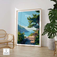 Framed Busan South Korea travel poster with coastal landscape, styled in modern room with chair and plant
