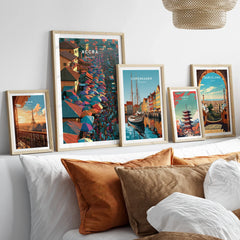 Set of five framed travel art prints including Accra Ghana above a bed in natural wood frames