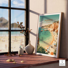 Algarve Beach Poster displayed on a wooden table by a window, featuring vintage design and pastel colors, showcasing Portugal's beautiful shores.