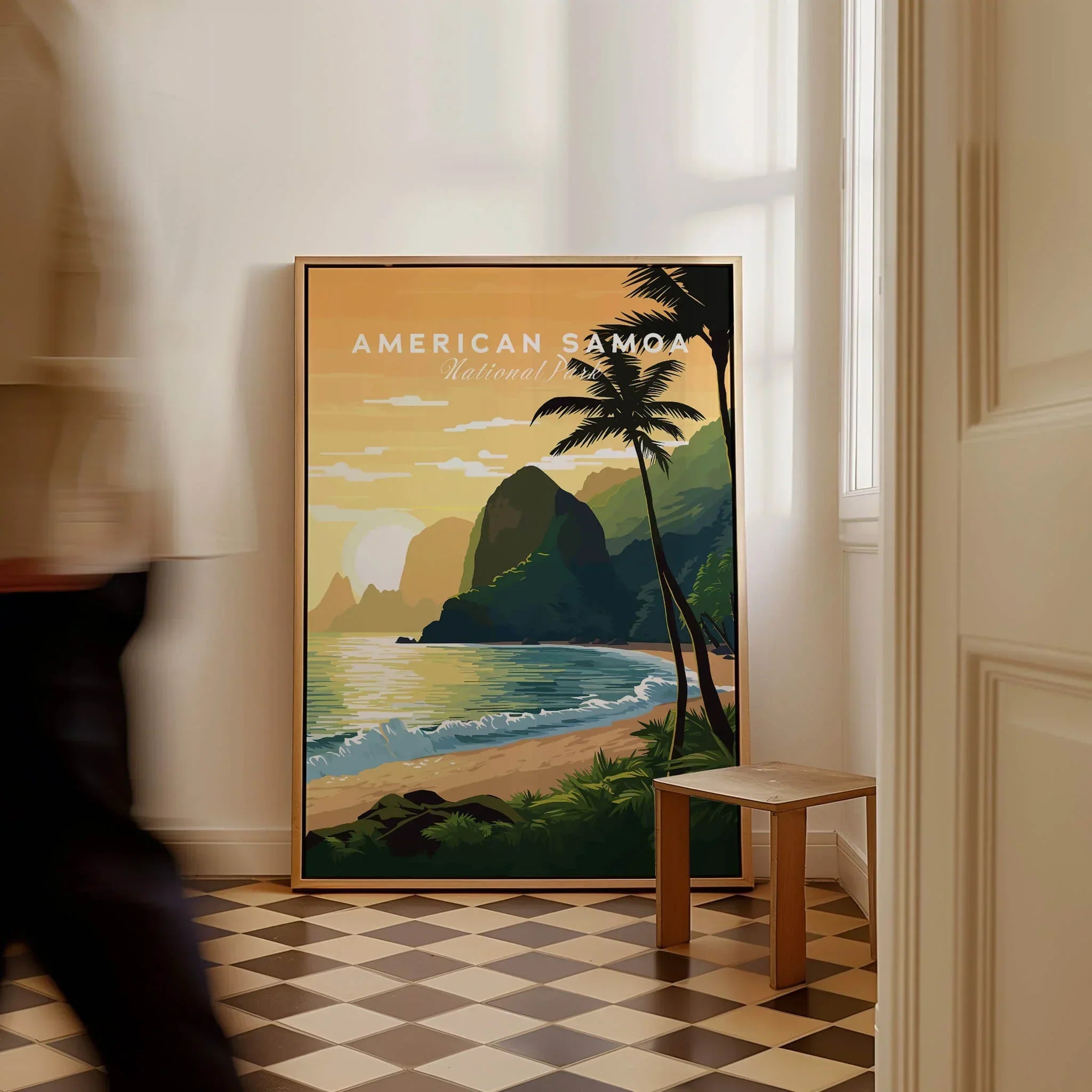 Framed American Samoa National Park travel poster with tropical beach art on a floor in a bright room, man walking past.