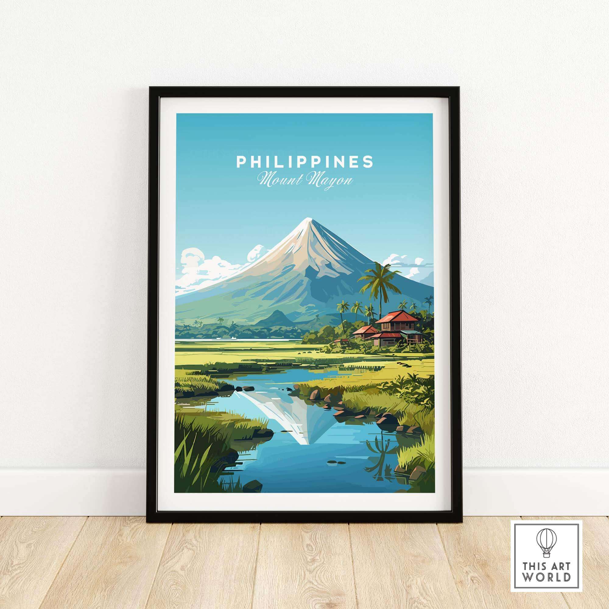 Travel poster of Mount Mayon in the Philippines with blue sky and tropical landscapes. The poster is shown framed in a black wooden frame resting on a natural wooden floor and leaning against a white wall. 