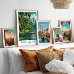 Framed travel posters of Paris, Bocas del Toro, Copenhagen, Tokyo, and Barcelona displayed above a cozy bed with pillows.