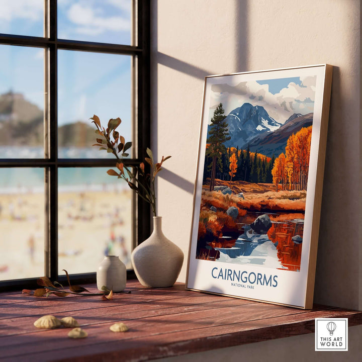 Cairngorms travel poster featuring vibrant autumn scenery and mountains, displayed on a wooden table by a sunny window.