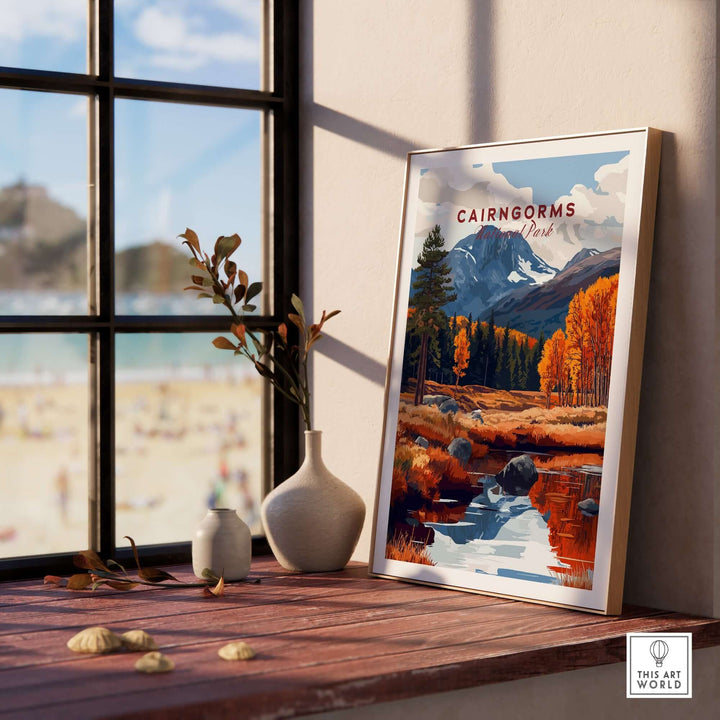 Cairngorms travel print displayed on a wooden table beside a vase, capturing autumn colors and mountain scenery.